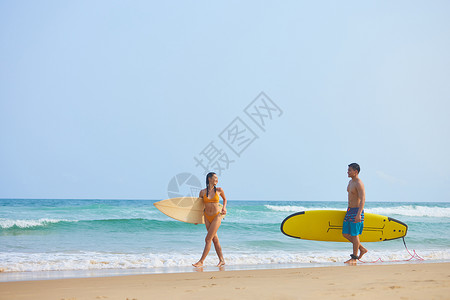 冲浪的情侣青年男女拿着冲浪板海边行走背景