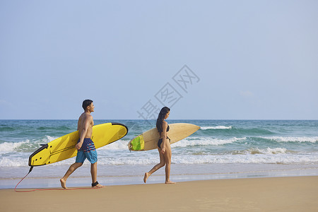 沙滩裤年轻男女拿着冲浪板海边行走背影背景