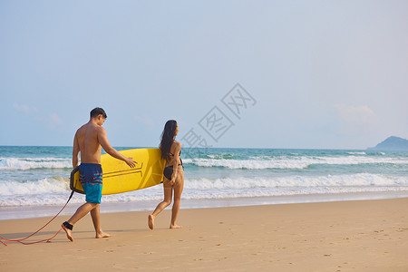 冲浪的情侣年轻男女拿着冲浪板海边行走背影背景