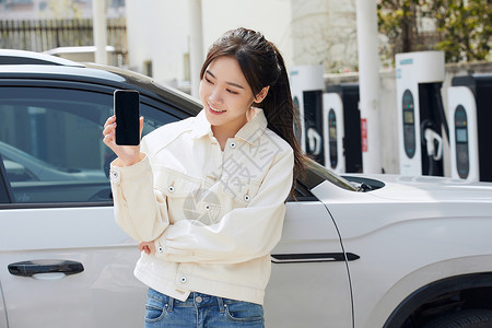 女性站在新能源汽车旁拿着手机图片