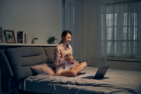 年轻女性坐在床上吃爆米花看电影图片