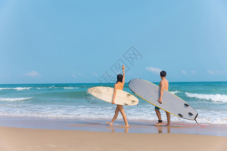划冲浪板情侣拿着冲浪板海边沙滩上行走背景