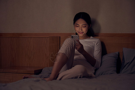 床头玩手机青年女性深夜睡前躺床上玩手机背景