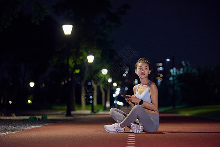 夜晚在公园健身的人坐在跑道上休息高清图片