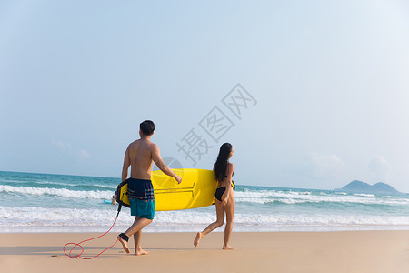 冲浪的情侣青年情侣拿着冲浪板海边沙滩上行走背景