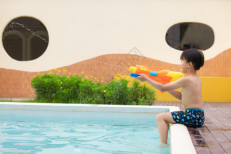 小男孩坐在泳池边玩水枪玩具背景