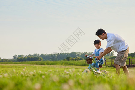 爸爸骑自行车年轻爸爸陪伴小男孩学骑自行车背景