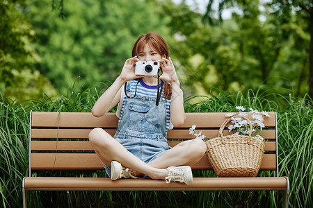 手拿相机坐在长椅上的夏日美女高清图片