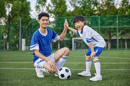 踢足球男孩足球教练和男孩在足球场踢球形象背景