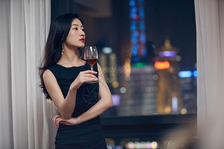 气质美女夜晚端着红酒杯站在窗前背景