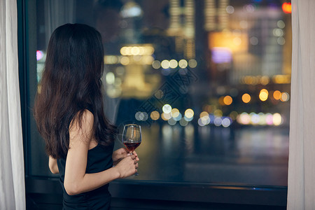饮酒派对美女夜晚端着红酒杯站在窗前背影背景