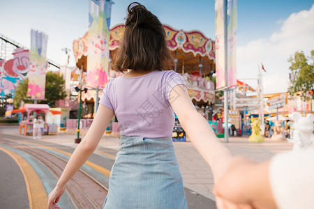 牵着男朋友手奔向游乐场的年轻女孩背影背景图片