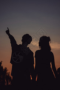 夕阳下的情侣指着远方天空剪影背景图片