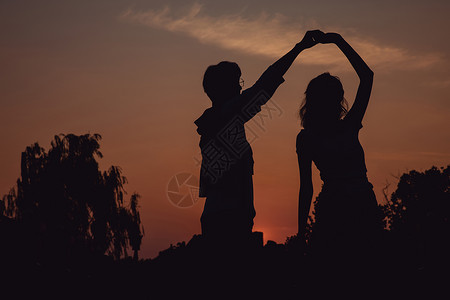 夕阳下牵手舞蹈的情侣剪影高清图片