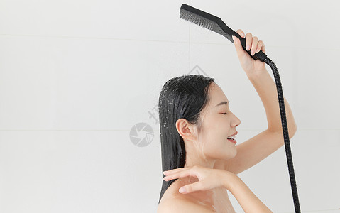 青年女性手拿花洒冲洗头发背景图片