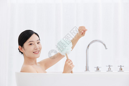 女性躺在浴缸手拿浴球刷洗澡图片