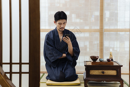 日式男青年喝茶玩手机背景图片