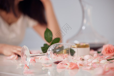 女性失落桌子上散落的玫瑰花和酒杯特写背景