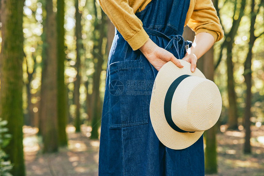 女性手拿草帽在森林里背影特写图片