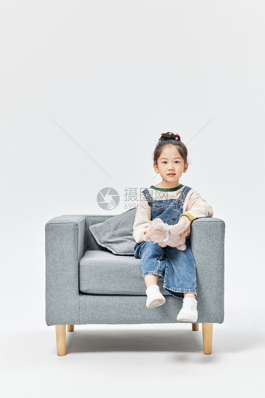小女孩居家坐沙发上玩绒毛玩具图片