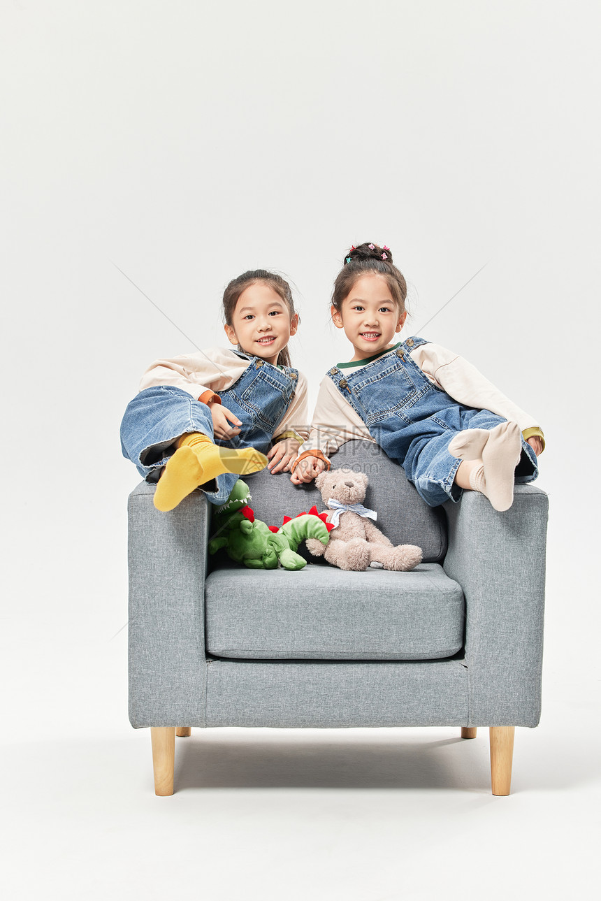 儿童双胞胎小女孩坐沙发上玩绒毛玩偶图片