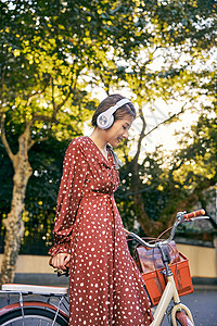 温暖秋季少女清新美女靠在自行车边上听着音乐背景
