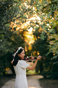 森林音乐夕阳余晖中拉小提琴的少女背景