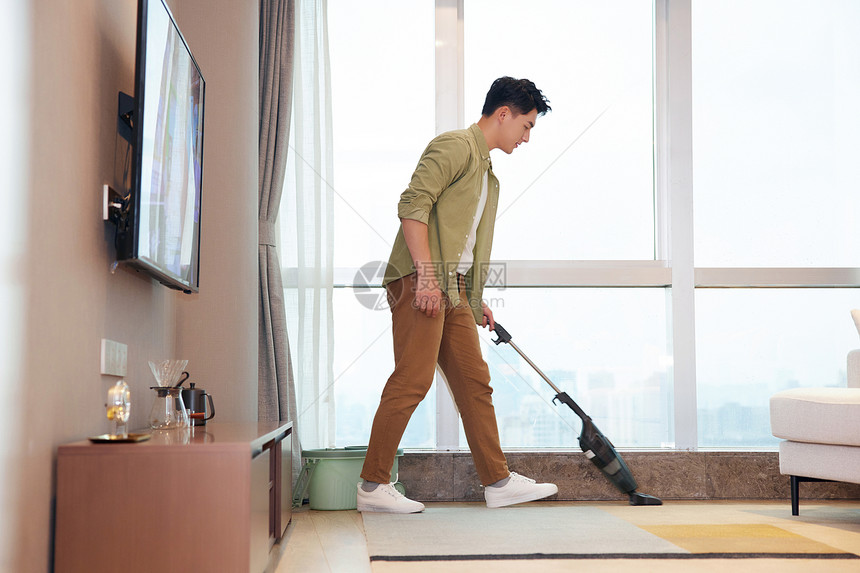 年轻男性居家使用吸尘器清洁地毯图片