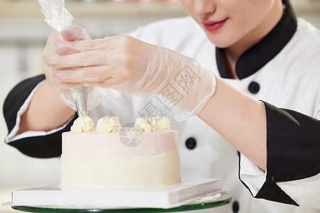 手绘女厨师青年女西点师为蛋糕裱花特写背景