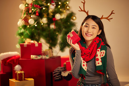 圣诞节人像美女圣诞节手拿礼物坐在圣诞树和礼物前背景
