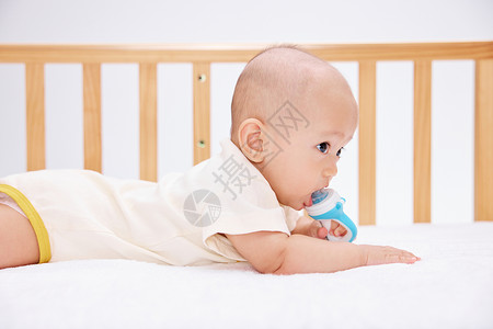 可爱宝宝在婴儿床里吃奶嘴爬行图片