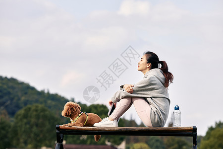 放空坐在长椅上的运动少女和萌宠泰迪背景