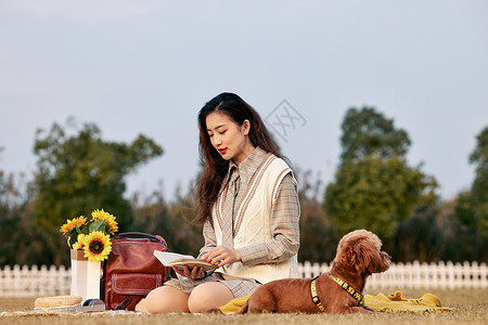 草地上睡觉的狗和看书的美女图片素材