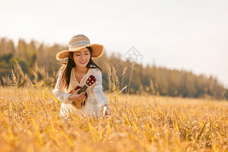 手拿尤克里里走在稻田的年轻女性图片