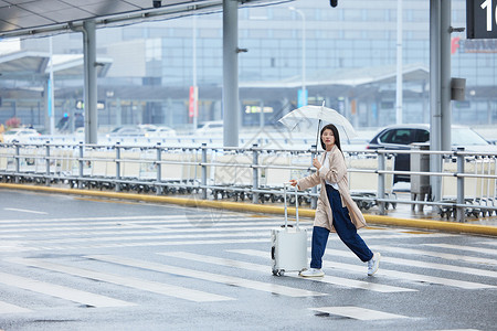 下雨天撑伞在机场外拉着行李的女性背景图片