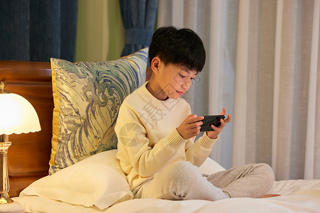 冬季夜晚小男孩睡前躺在床上玩手机背景