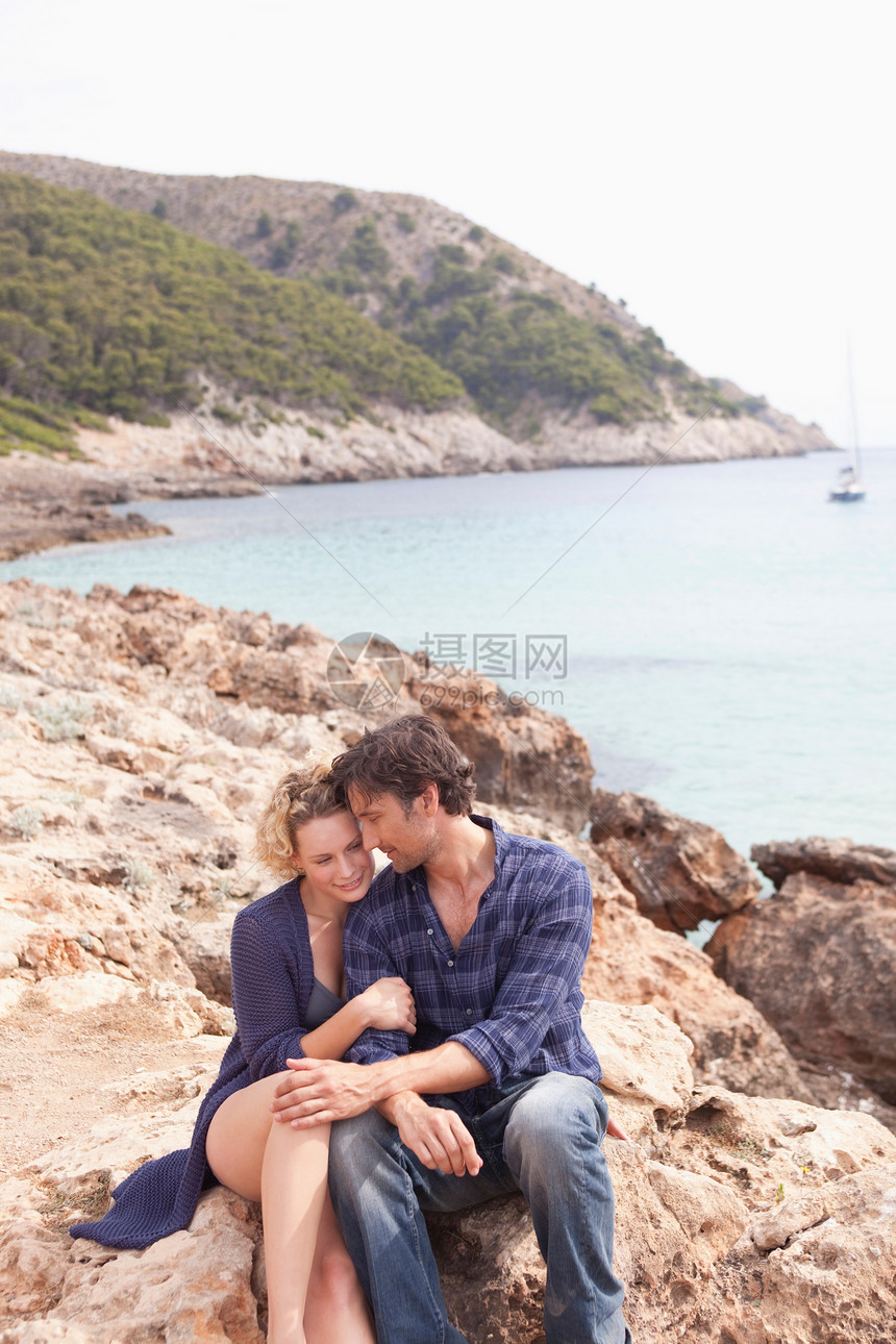 在海滩的岩石上坐着一对情侣图片