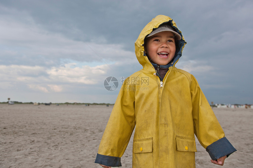 微笑的男孩在海滩上穿着雨衣图片