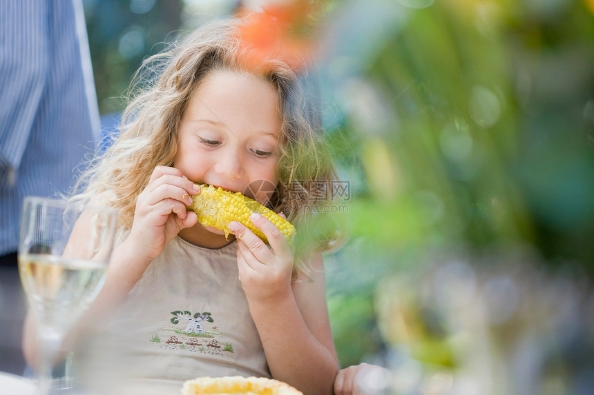 女孩在户外餐桌上吃玉米图片