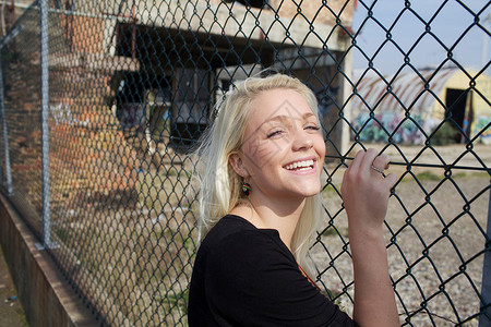 微笑的女孩靠着栅栏站立着图片