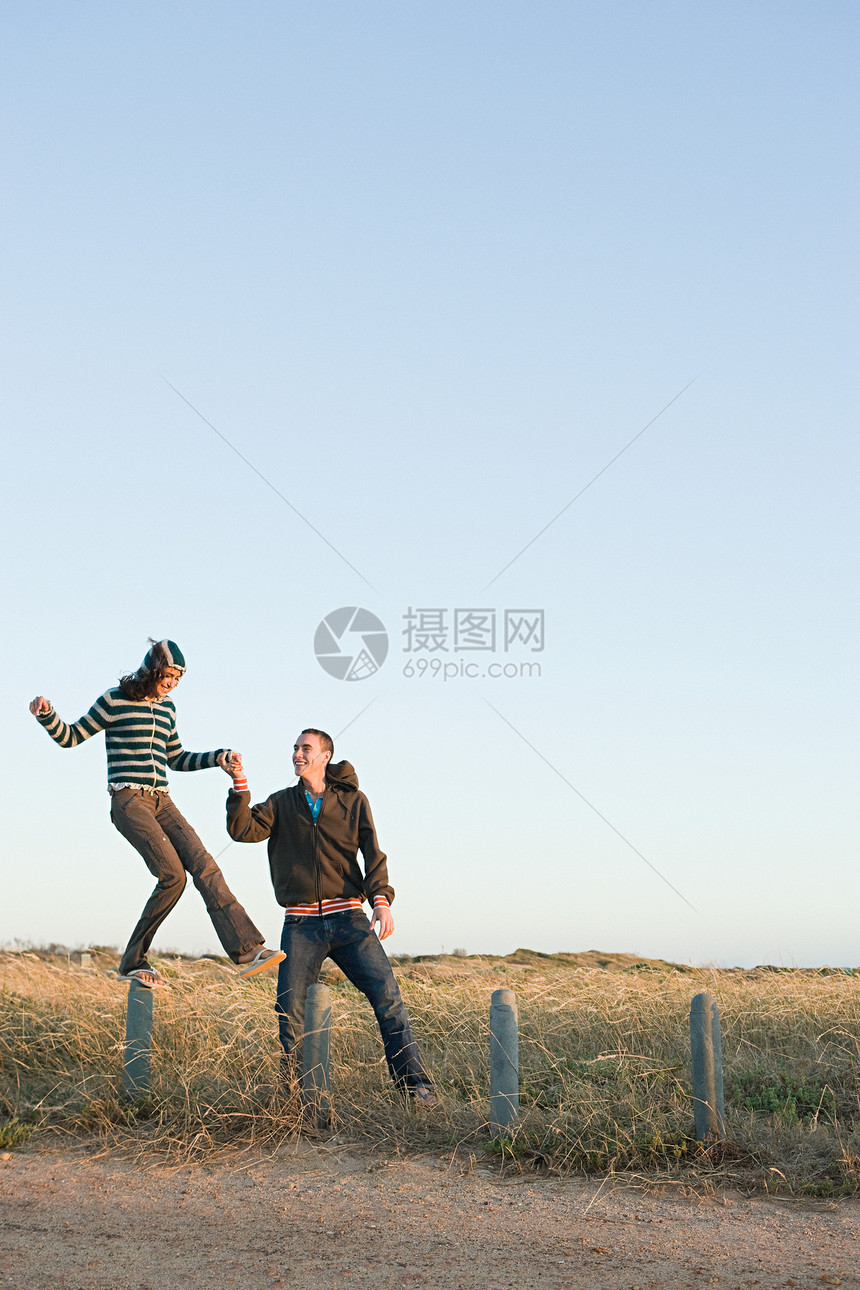 一个年轻男子帮助一个女人平衡在栅栏上图片