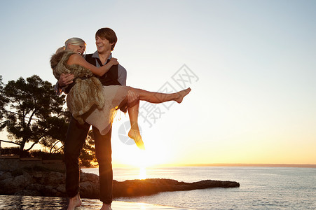 男人在日落时带着女朋友在海边图片