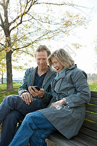 在公园长椅上看手机的母亲和成年儿子图片