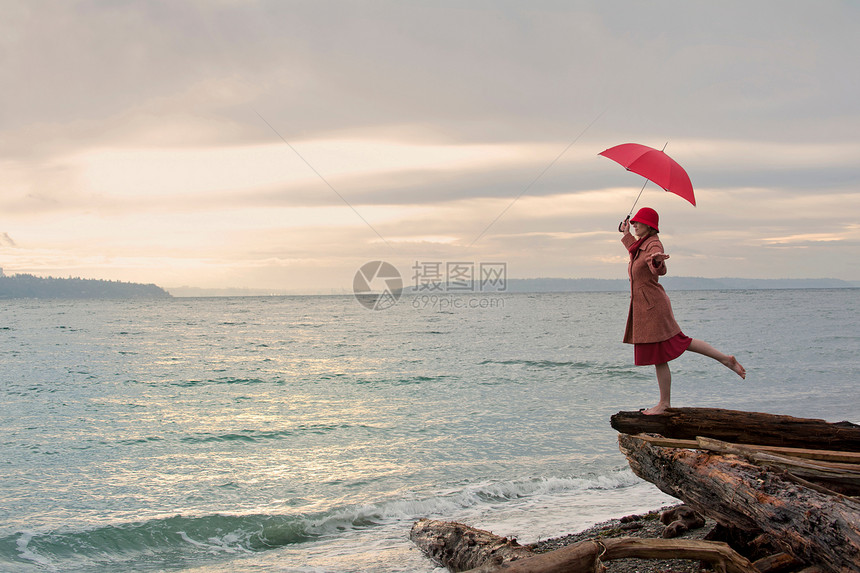 海边悬崖上撑着雨伞的女性图片