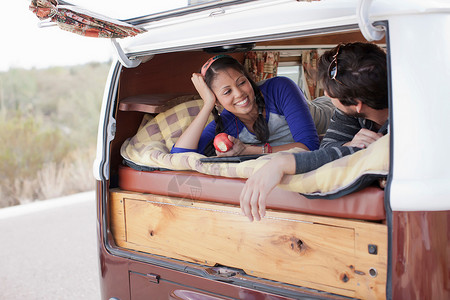 一对夫妇躺在露营面包车后备箱图片
