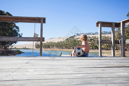 男孩与足球坐在码头上图片