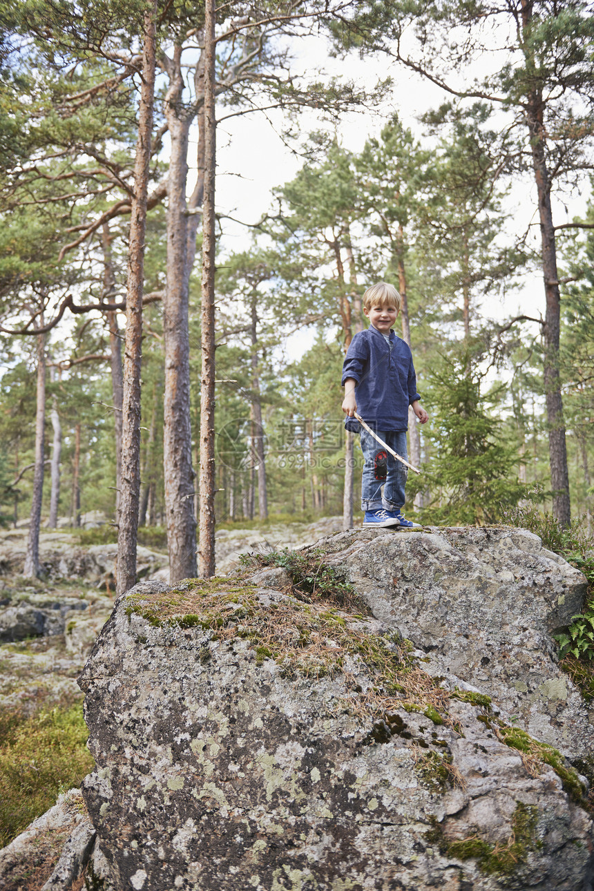 男孩站在岩石上握着棍棒图片