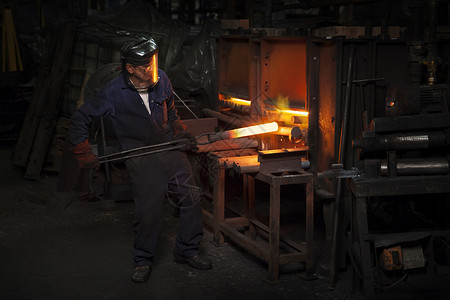 工厂内工人夹起烧红的铁块高清图片
