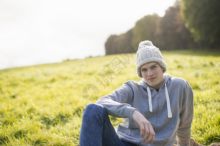 戴着针织帽坐在草地上的年轻人 图片