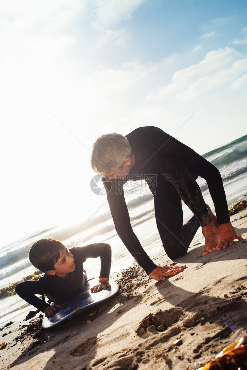 海滩上教儿子使用冲浪板的父亲图片